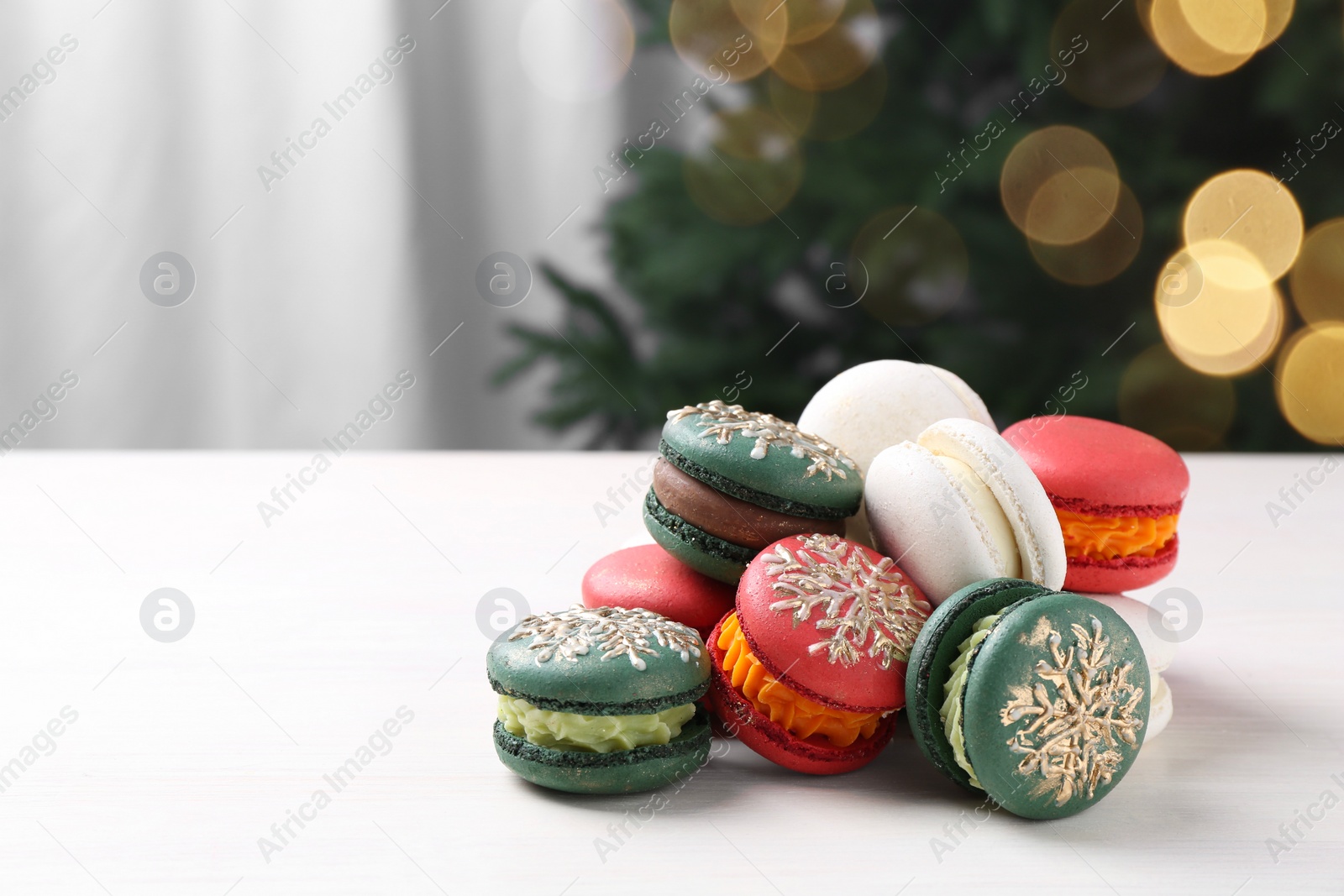 Photo of Different decorated Christmas macarons on white table indoors, space for text