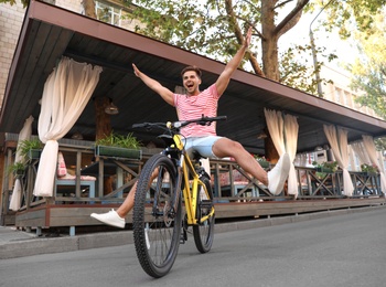 Handsome young man riding bicycle on city street, low angle view