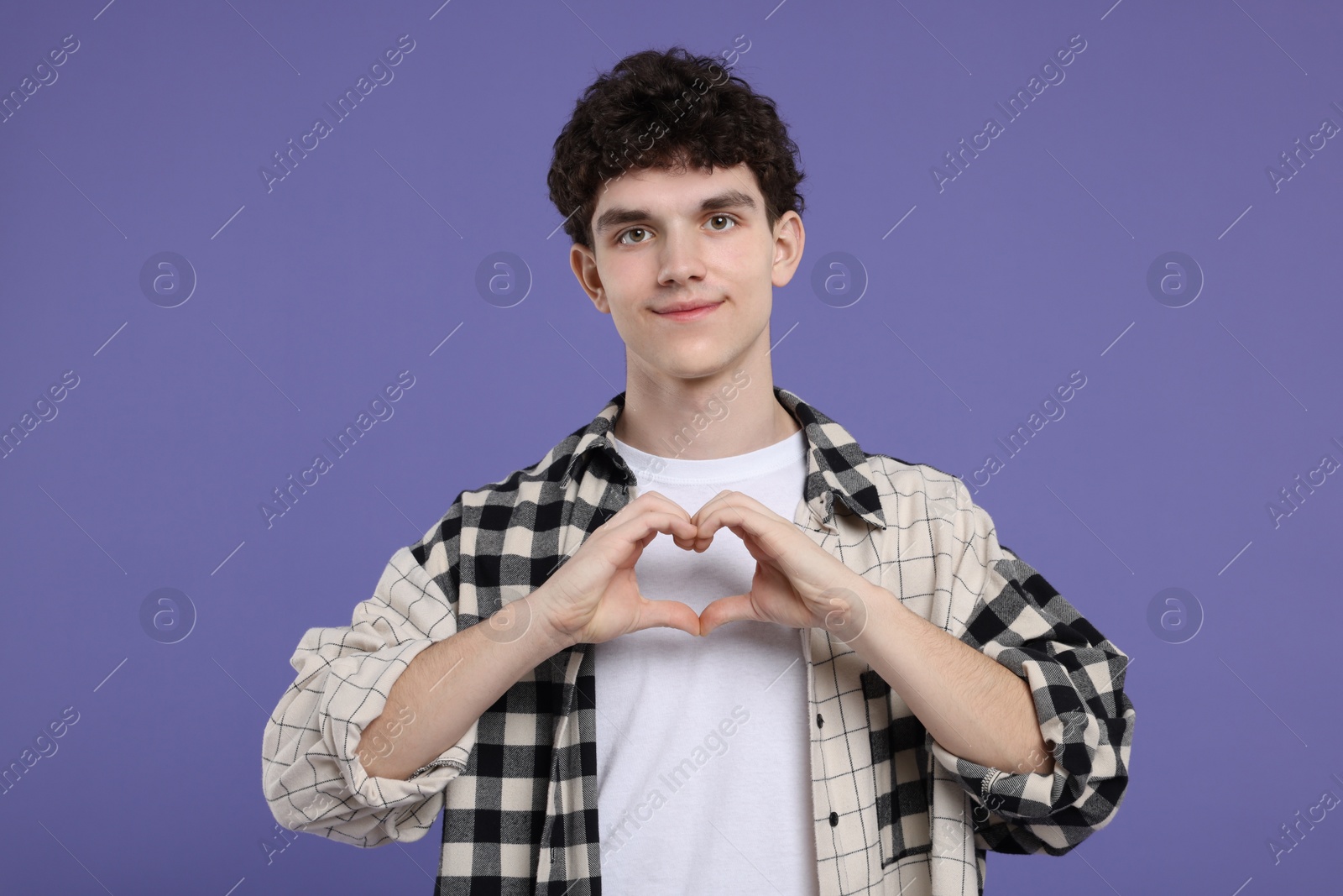 Photo of Happy young man showing heart gesture with hands on purple background