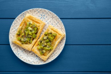 Photo of Fresh tasty puff pastry with kiwi on blue wooden table, top view. Space for text