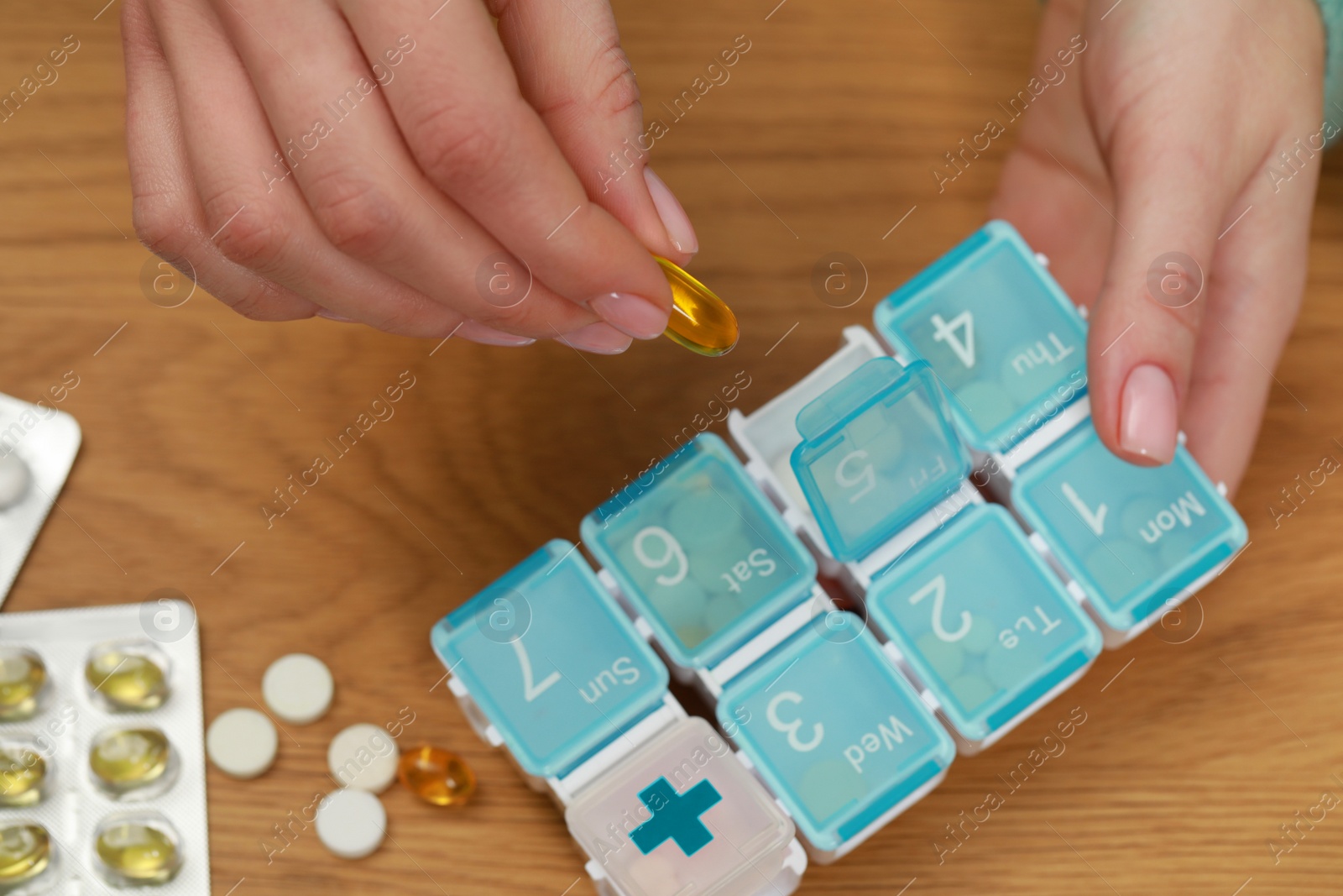 Photo of Woman taking pill from plastic box at wooden table, top view