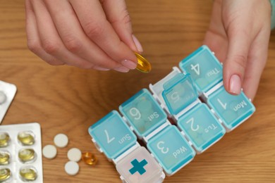 Woman taking pill from plastic box at wooden table, top view