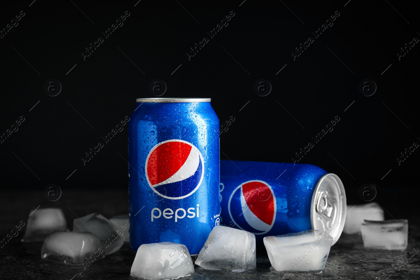 Photo of MYKOLAIV, UKRAINE - FEBRUARY 11, 2021: Cans of Pepsi with water drops and ice cubes on grey table against black background