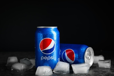 MYKOLAIV, UKRAINE - FEBRUARY 11, 2021: Cans of Pepsi with water drops and ice cubes on grey table against black background