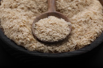 Photo of Bowl and spoon of brewer`s yeast flakes on black background, closeup