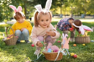 Photo of Cute little children hunting eggs in park. Easter tradition