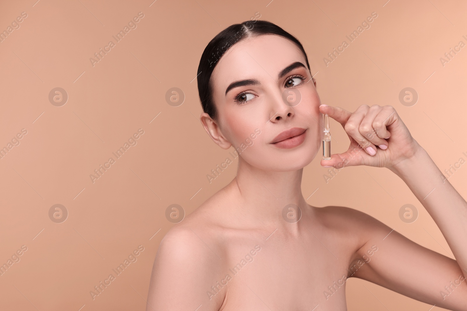 Photo of Beautiful young woman holding skincare ampoule on beige background. Space for text