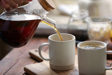 Photo of Pouring delicious tea into cup on wooden table, closeup