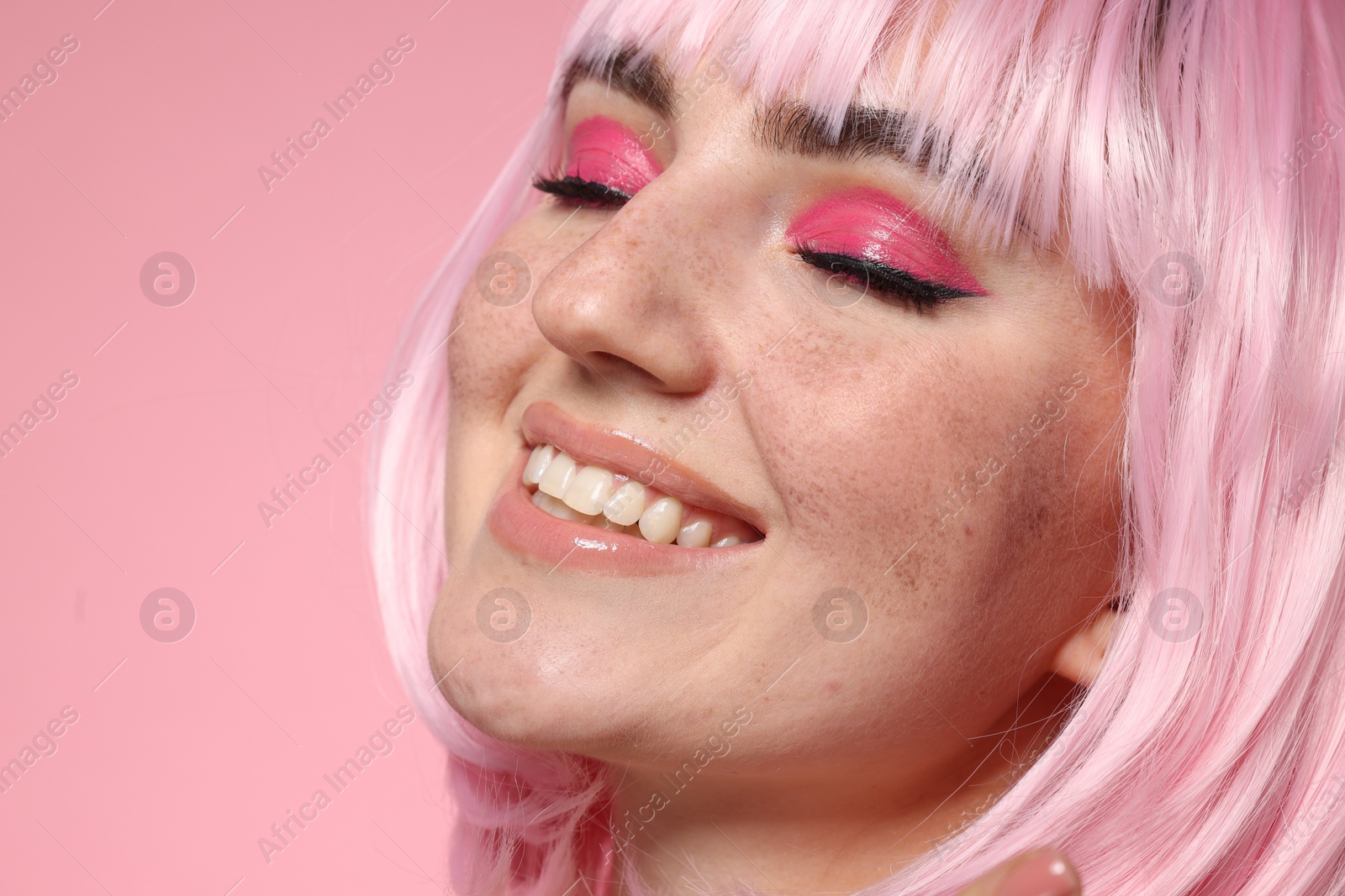 Photo of Smiling woman with bright makeup and fake freckles on pink background, closeup. Space for text