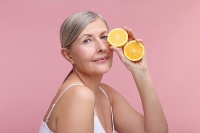 Photo of Beautiful woman with halves of orange rich in vitamin C on pink background