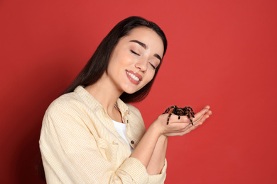Photo of Woman holding striped knee tarantula on red background. Exotic pet