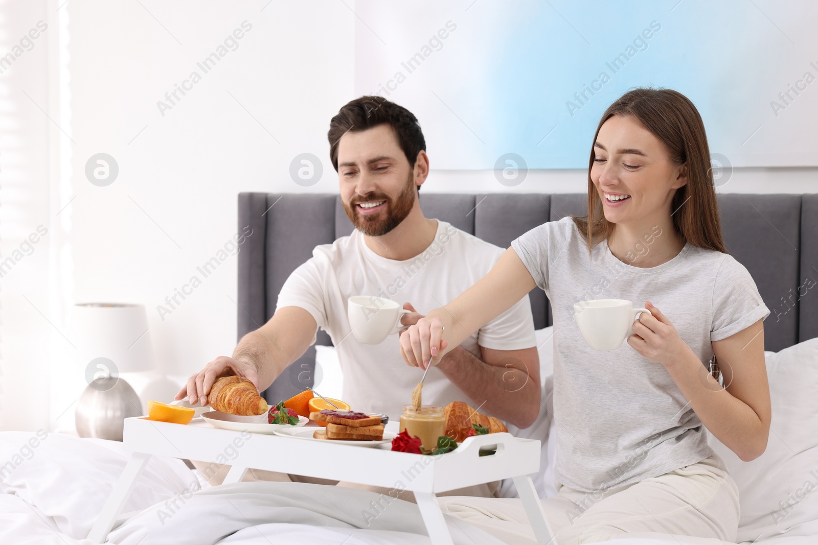 Photo of Happy couple eating tasty breakfast on bed at home