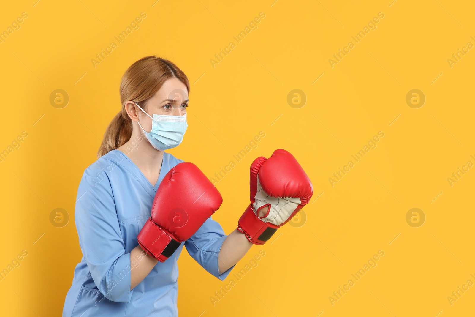 Photo of Doctor with protective mask and boxing gloves on yellow background, space for text. Strong immunity concept