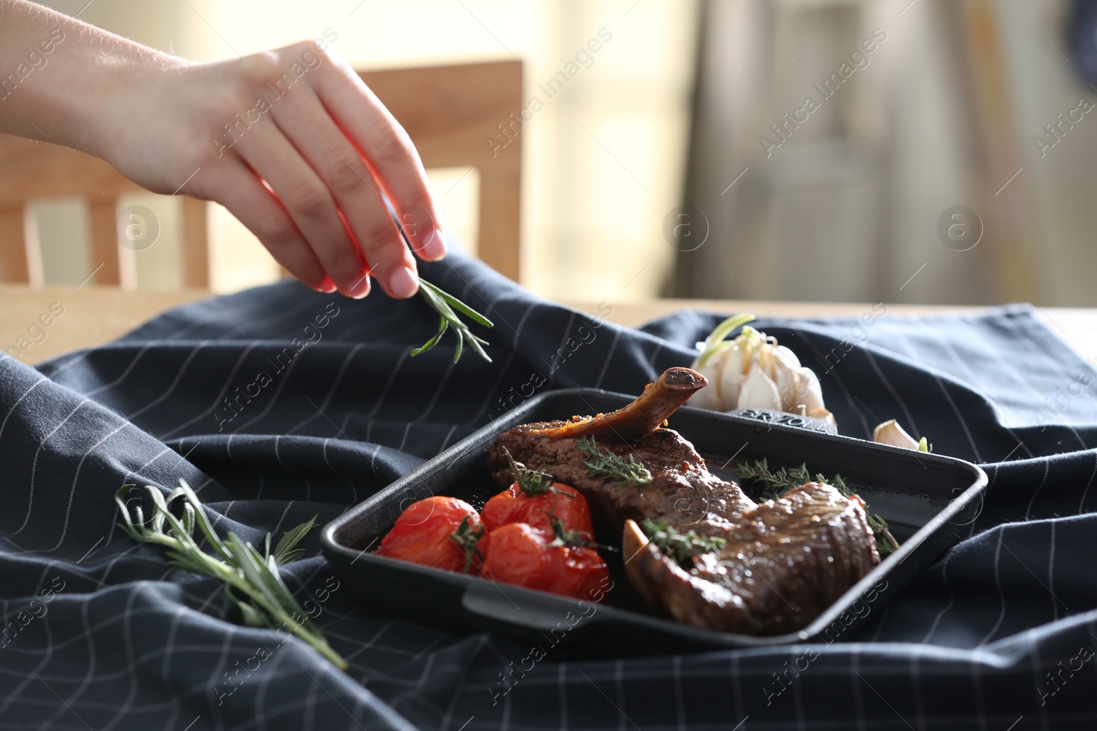 Photo of Woman adding rosemary to roasted ribs at table, closeup