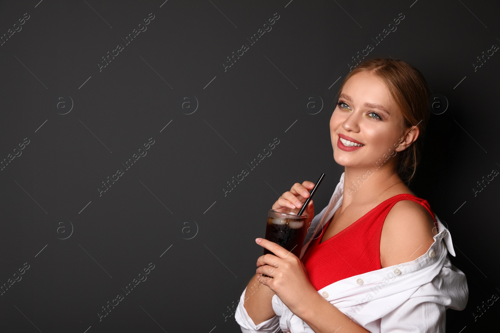 Photo of Young woman with glass of cola on black background, space for text. Refreshing drink