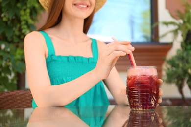 Photo of Woman with glass of natural detox lemonade at table in outdoor cafe, closeup