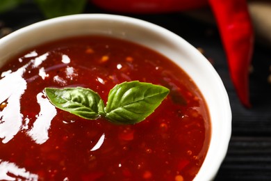 Photo of Spicy chili sauce with basil on dark table, closeup