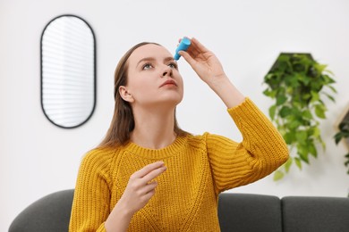 Young woman applying medical eye drops indoors