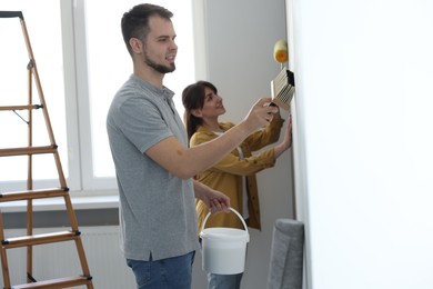 Photo of Man and woman hanging wallpaper in room