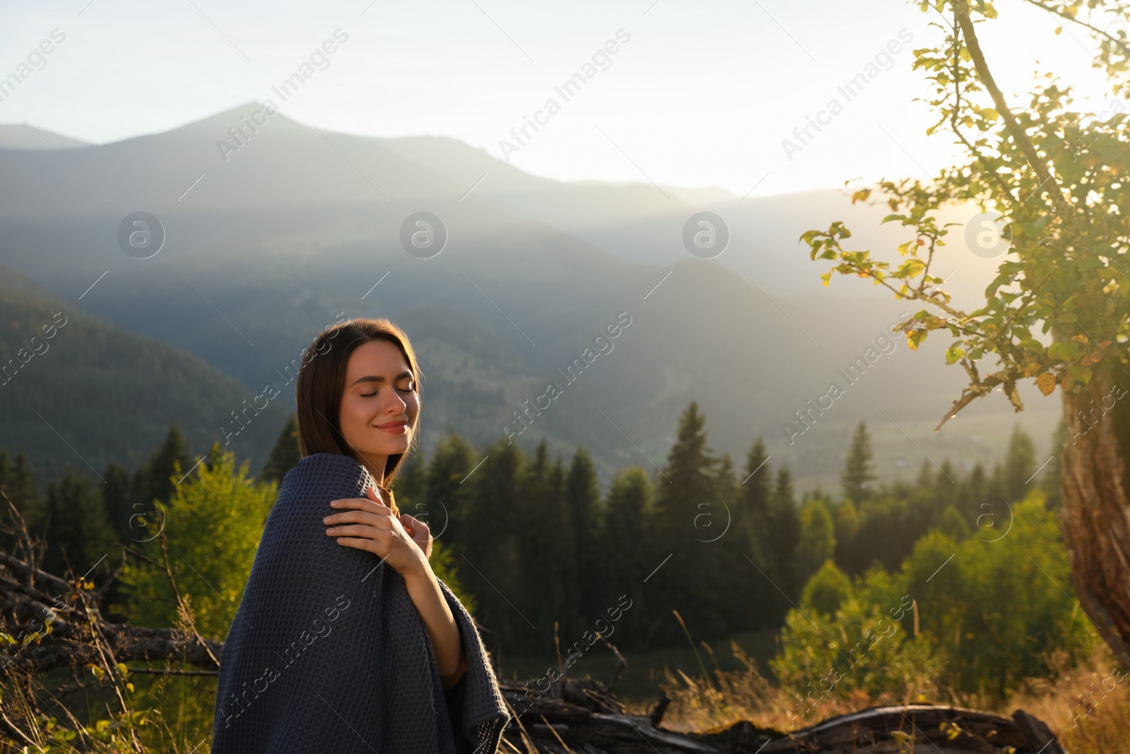 Photo of Woman with cozy plaid enjoying warm sunlight in mountains