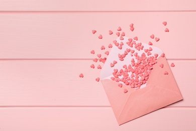 Photo of Heart shaped sprinkles with envelope on pink wooden table, flat lay. Space for text