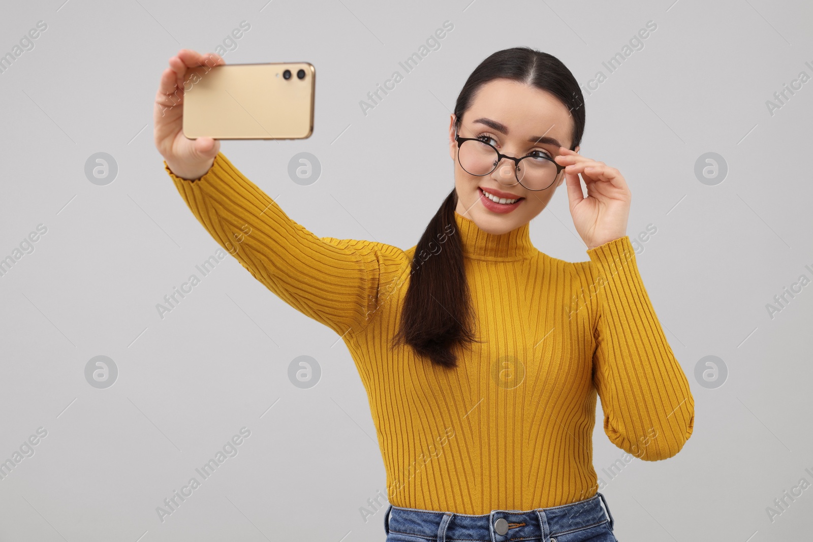 Photo of Smiling young woman taking selfie with smartphone on grey background
