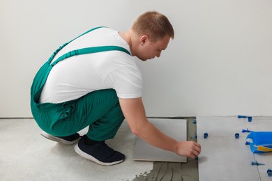 Photo of Worker installing ceramic tile on floor near wall