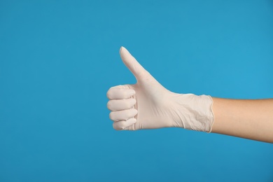 Photo of Doctor in medical gloves showing thumb up on light blue background, closeup