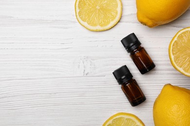 Bottles of citrus essential oil and fresh lemons on white wooden table, flat lay. Space for text