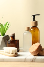 Photo of Different bath accessories and houseplant on wooden table against beige background