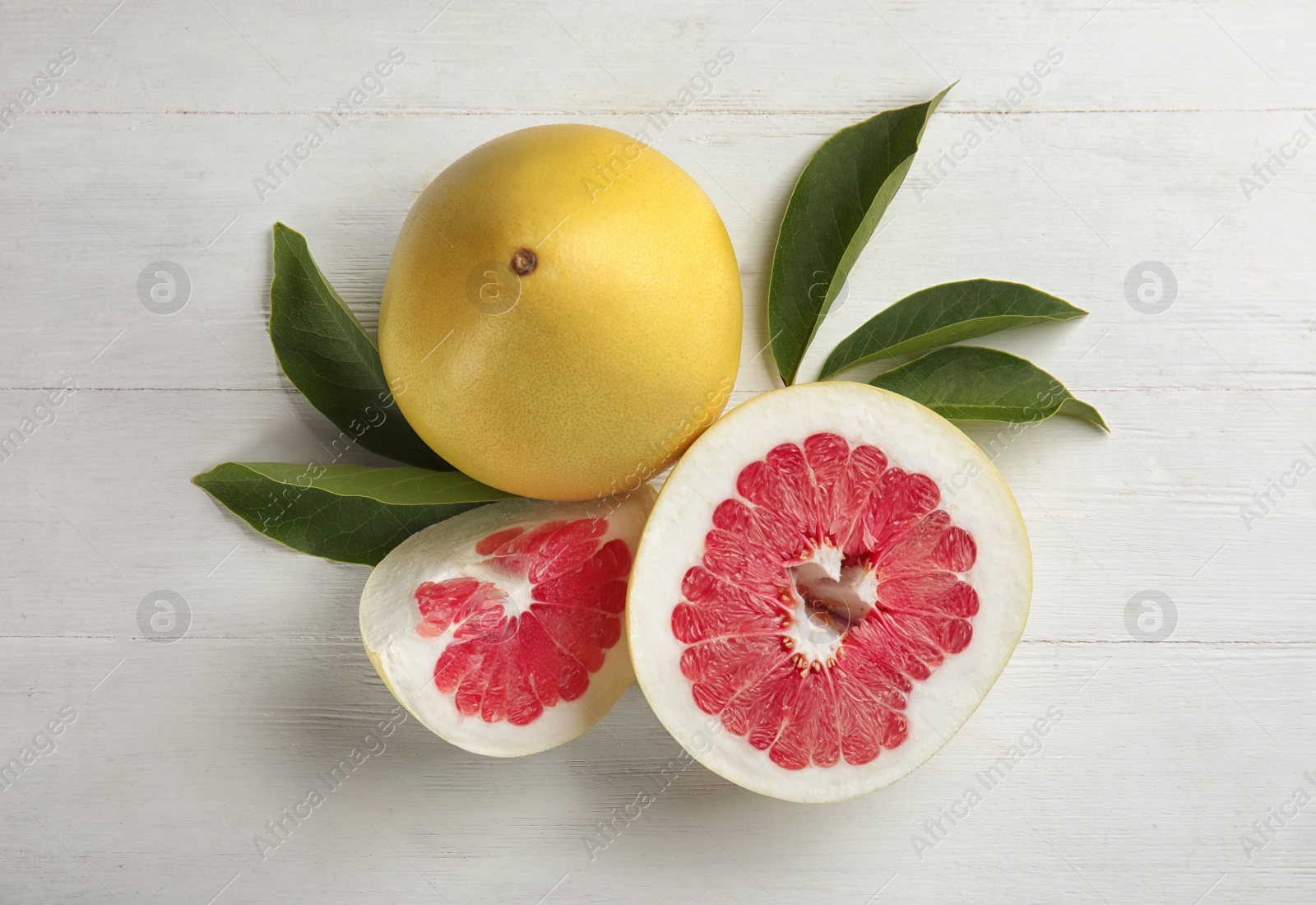 Photo of Fresh cut and whole pomelo fruits with leaves on white wooden table, flat lay