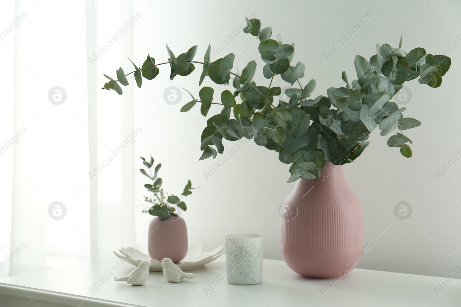 Photo of Beautiful eucalyptus branches, candle and bird figures on white table indoors. Interior element