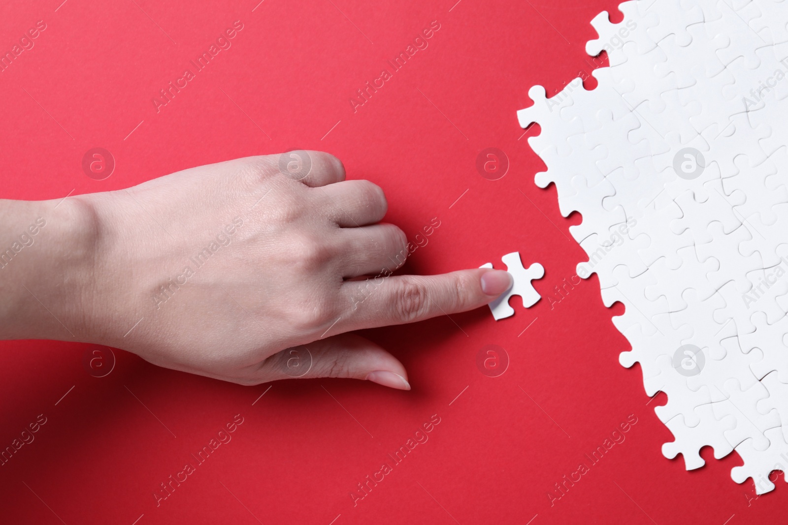 Photo of Woman putting together white puzzle on red background, closeup
