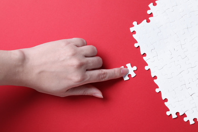 Woman putting together white puzzle on red background, closeup