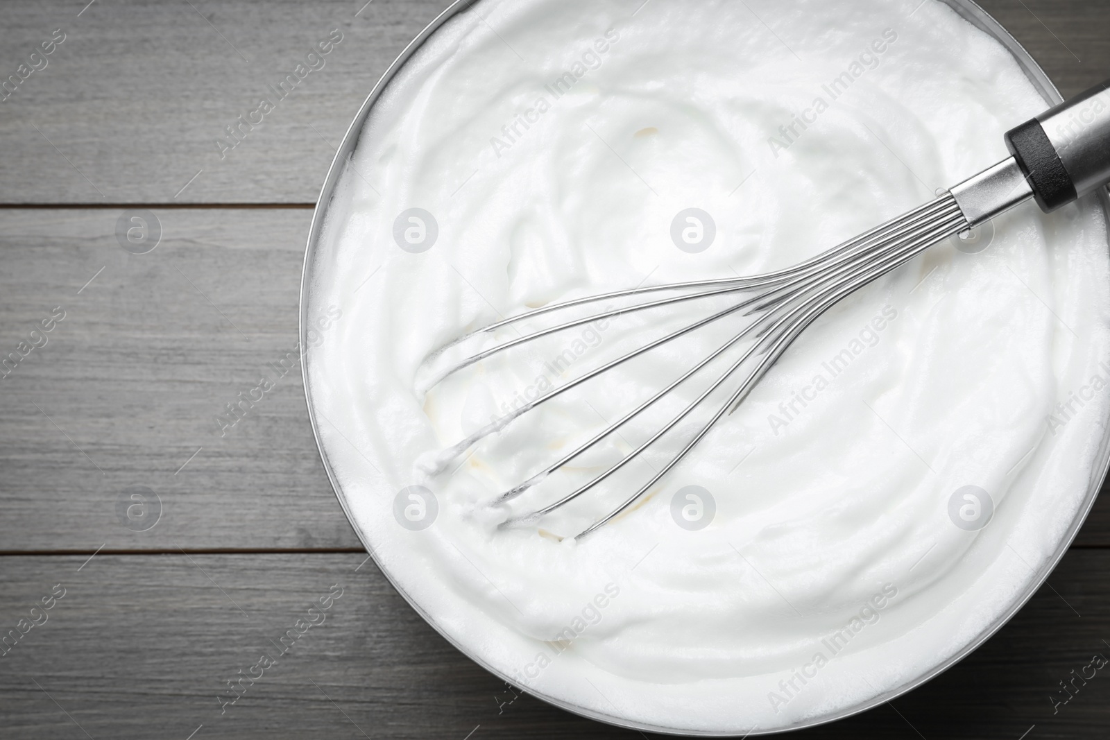 Photo of White cream with balloon whisk on grey wooden table, top view