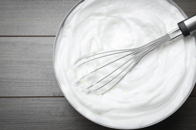 White cream with balloon whisk on grey wooden table, top view