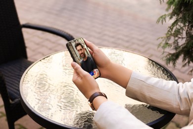 Image of Woman viewing male profile on dating site via mobile phone at outdoor cafe table, closeup