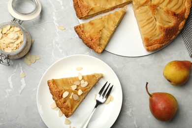 Photo of Cut delicious sweet pear tart and almond flakes on grey marble table, flat lay