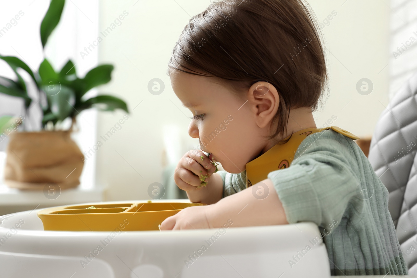 Photo of Cute little baby eating healthy food in high chair indoors