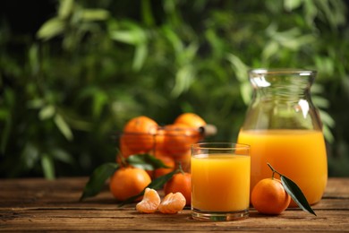 Photo of Glass and bottle of fresh tangerine juice and fruits on wooden table. Space for text