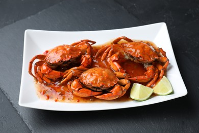 Photo of Delicious boiled crabs with sauce and lime on black textured table