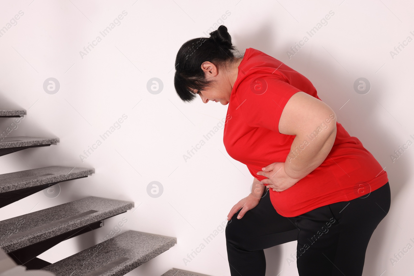 Photo of Overweight mature woman suffering from pain in left side while running upstairs indoors, space for text