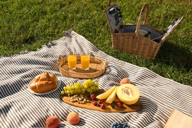 Picnic blanket with delicious food and juice on green grass outdoors