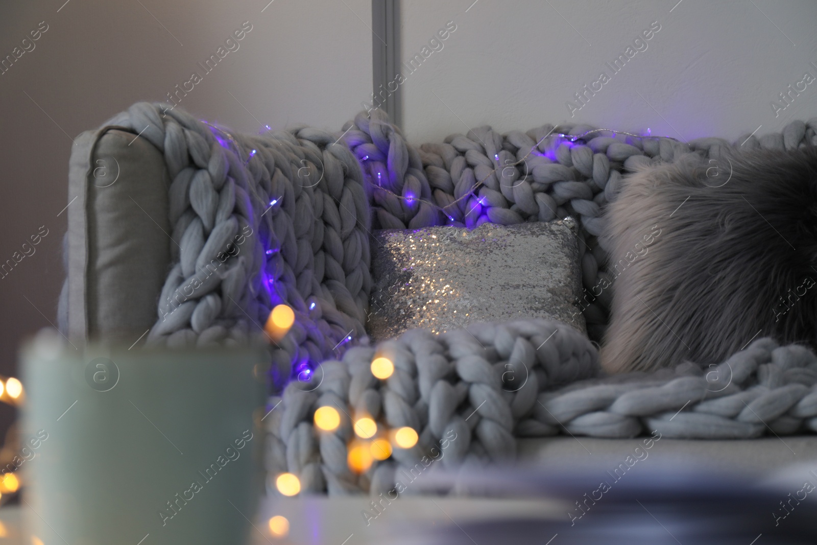 Photo of Comfortable sofa with plaid and Christmas lights in living room