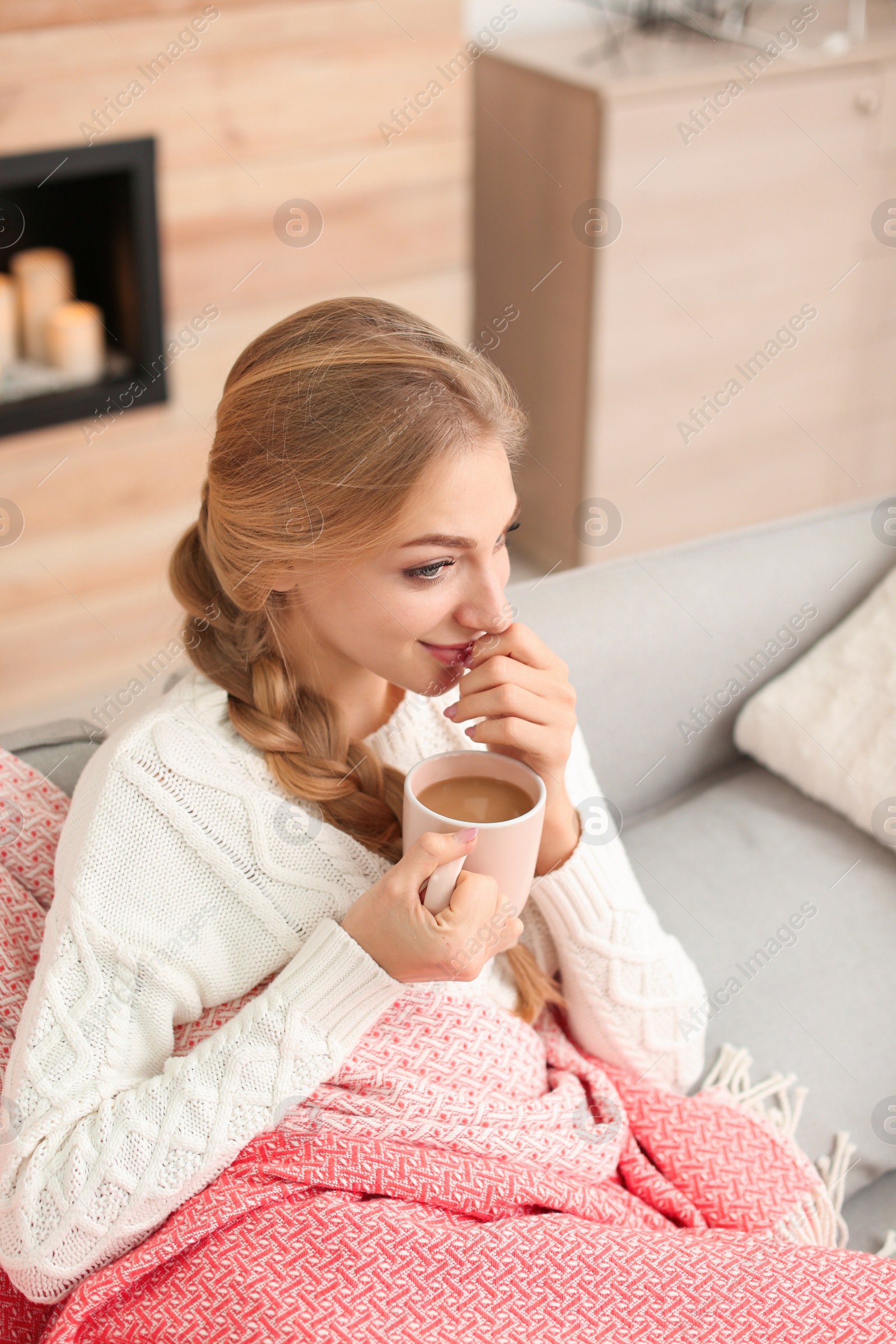 Photo of Beautiful young woman sitting on sofa with cup at home. Winter atmosphere