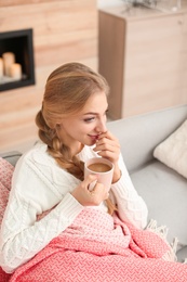 Beautiful young woman sitting on sofa with cup at home. Winter atmosphere