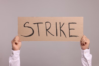 Photo of Man holding cardboard banner with word Strike on light grey background, closeup