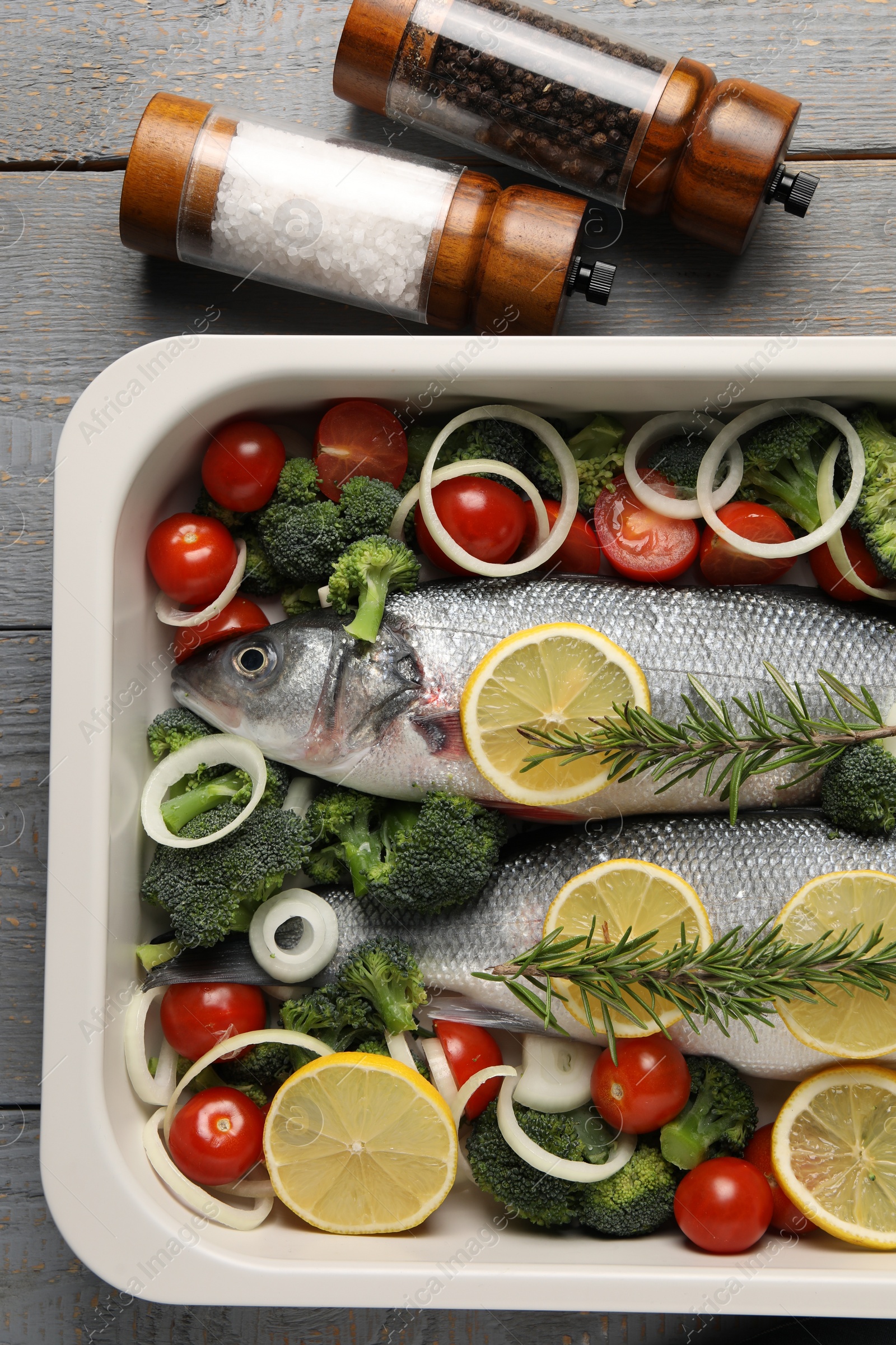 Photo of Raw fish with vegetables and lemon in baking dish and spices on grey wooden table, flat lay