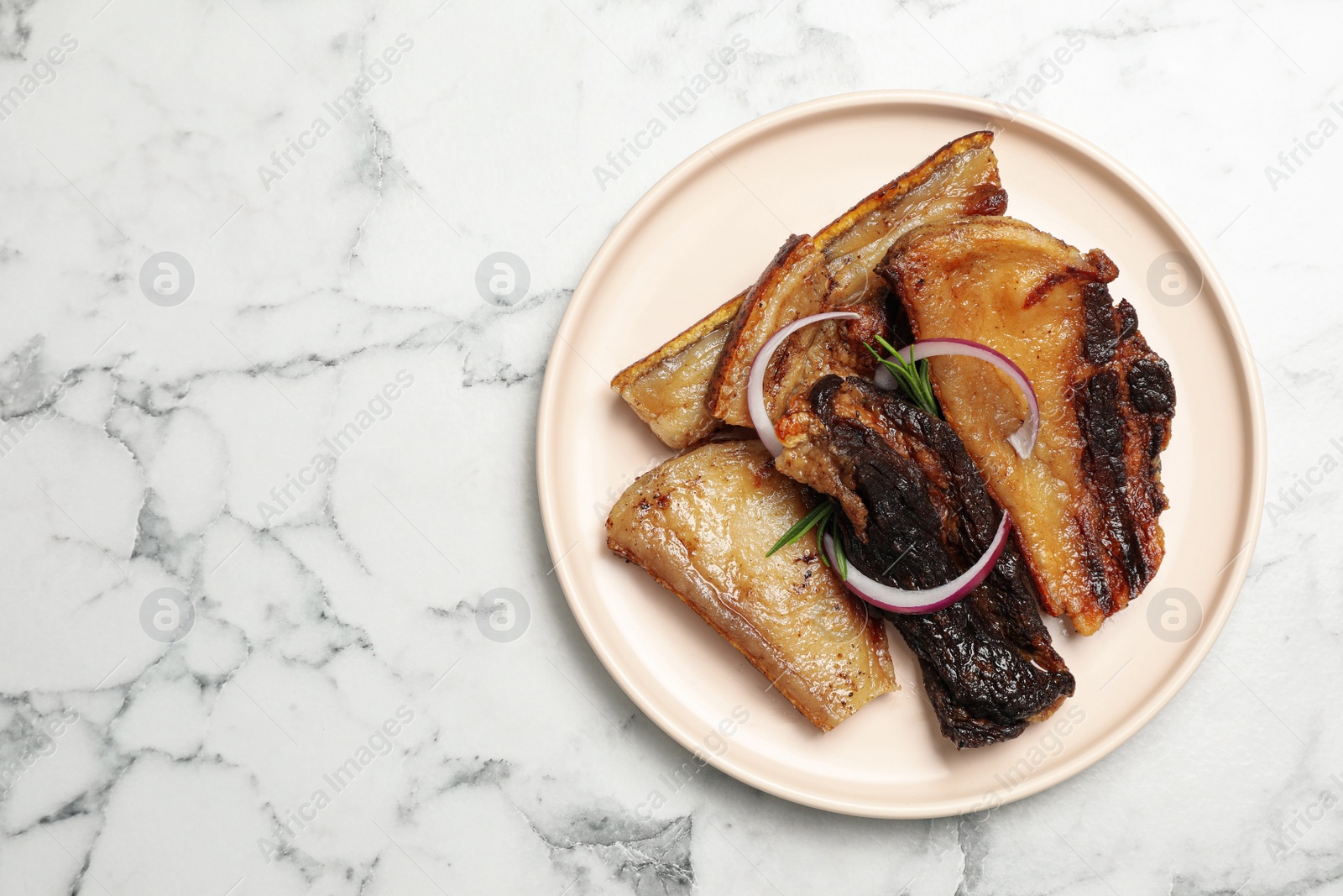 Photo of Tasty fried pork lard with rosemary and onion on white marble table, top view. Space for text