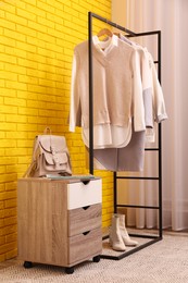 Rack with stylish clothes near yellow brick wall indoors